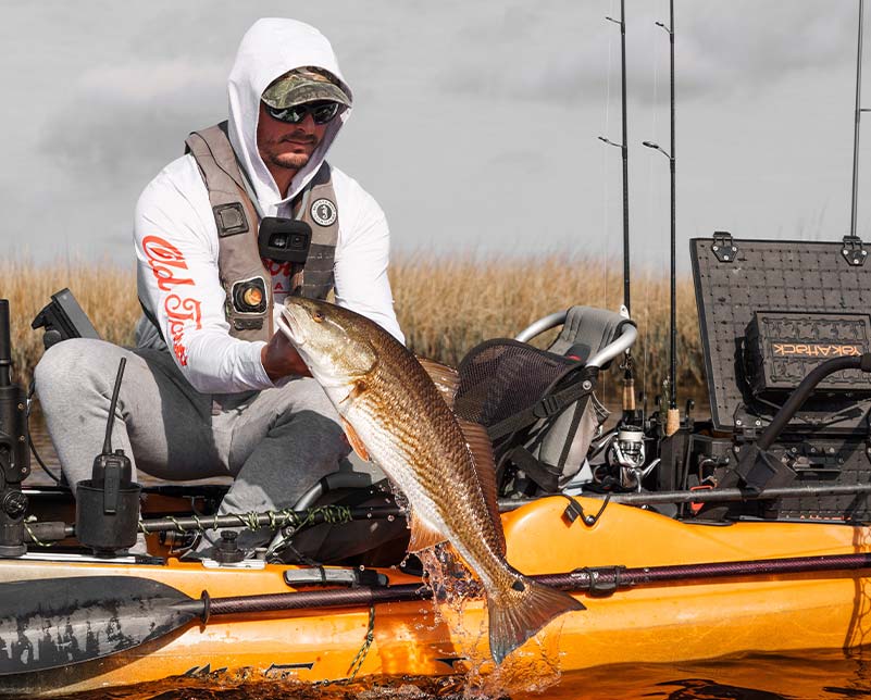 Man pulling up large fish from water caught in the Old Town Sportsman BigWater 132 fishing kayak